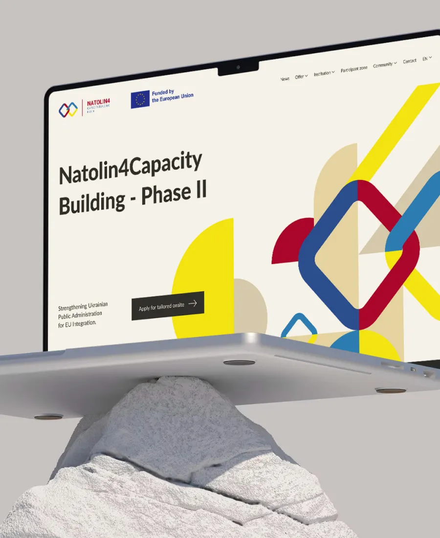 Laptop ze stroną projektu Natolin4Capacity Building balansujący na kamieniu, na szarym tle
