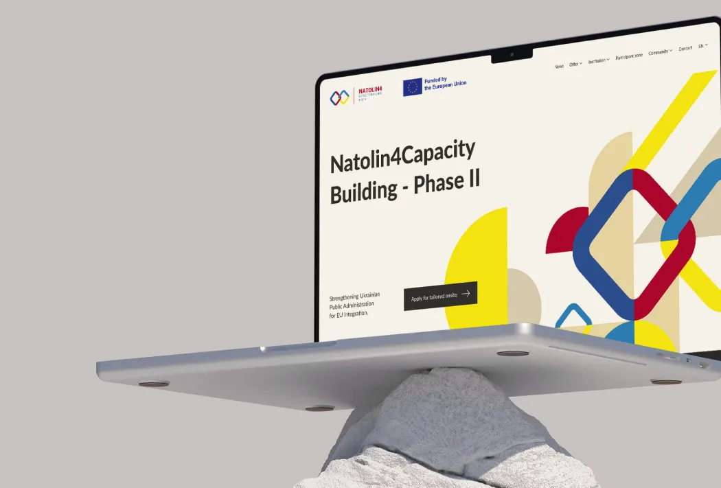 Laptop ze stroną projektu Natolin4Capacity Building balansujący na kamieniu, na szarym tle