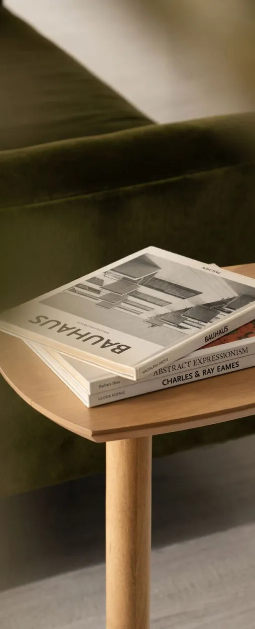 Albumy o Bauhausie i designie na drewnianym stoliku przy zielonej welurowej sofie