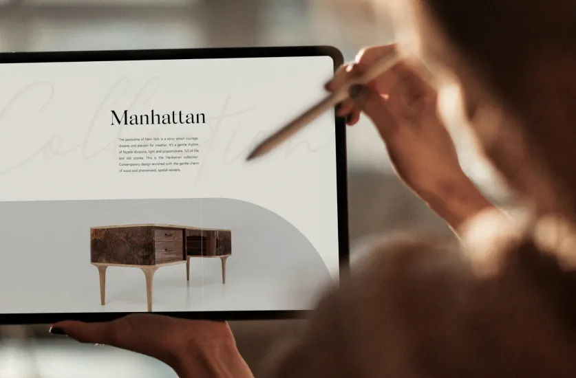 Dłonie z rysikiem trzymające tablet ze stroną kolekcji mebli „Manhattan”